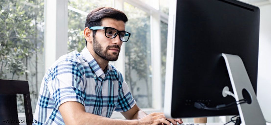 man wearing blue light glasses in front of computer